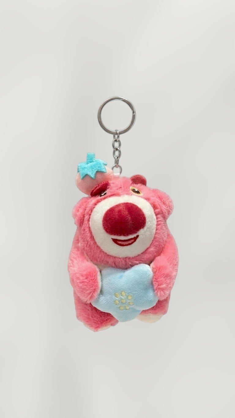 Tagerelsa3ada pink plush bear keychain with strawberry hat, holding a blue heart with embroidered flowers.