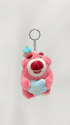 Tagerelsa3ada pink plush bear keychain with strawberry hat, holding a blue heart with embroidered flowers.
